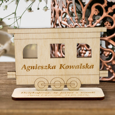 Aranżacja stołu weselnego z motywem kolejowym – drewniane winietki lokomotywa i wagon przy nakryciach.