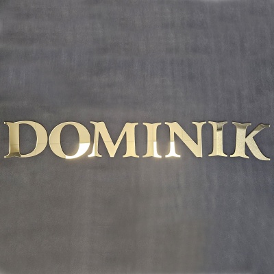 Eleganckie literki lustrzane złote z plexi o grubości 3 mm ułożone w personalizowany napis na ciemnym szarym tle.